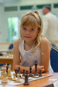 a girl sitting at a table with chess pieces